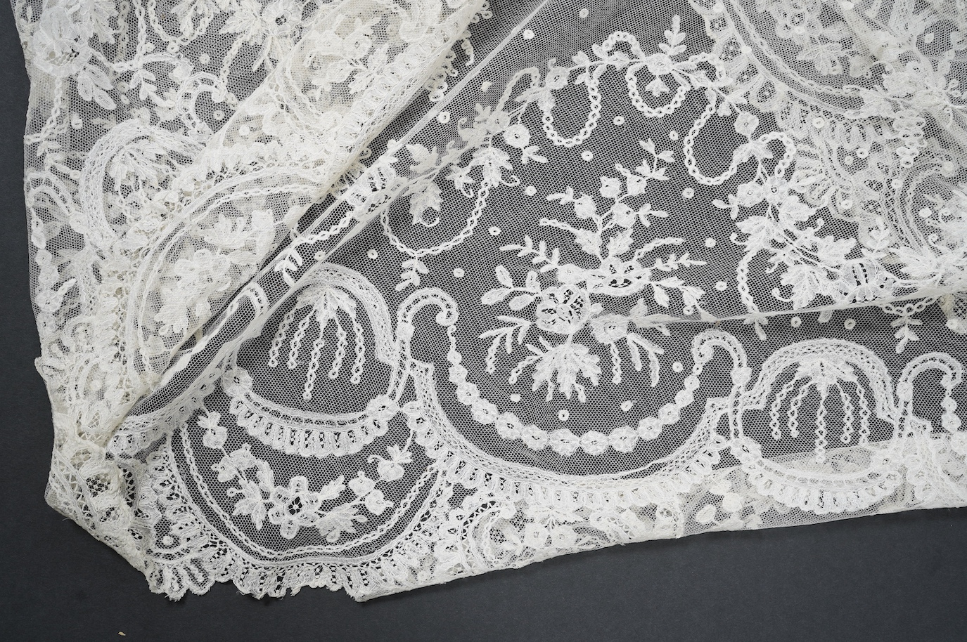 A wide flounce of fine ornate hand made 19th century Brussels bobbin lace, appliquéd onto a net ground, possibly commissioned for a wedding gown, now sewn together along the top edge and the two cut ends also stitched to